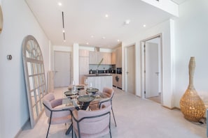 A modern kitchen with a central island, a dining area with a glass table and chairs, and a large decorative vase. - Czechin - Signature Livings (Madinat Zayed)