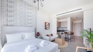 A modern hotel room with a large bed, a sofa, a coffee table, and a view of the kitchen and dining area. - Czechin - Signature Livings (Madinat Zayed)