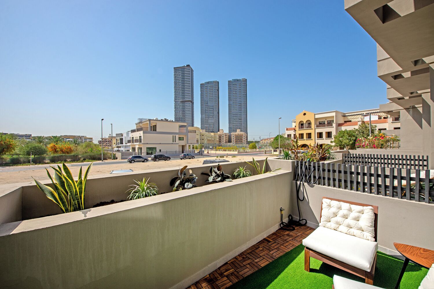 Un balcón con vistas a edificios altos, una silla blanca con cojines y una mesita.