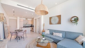 A modern living room with a glass coffee table, a blue sofa, and a dining area with a table and chairs. - Czechin - Signature Livings (Madinat Zayed)
