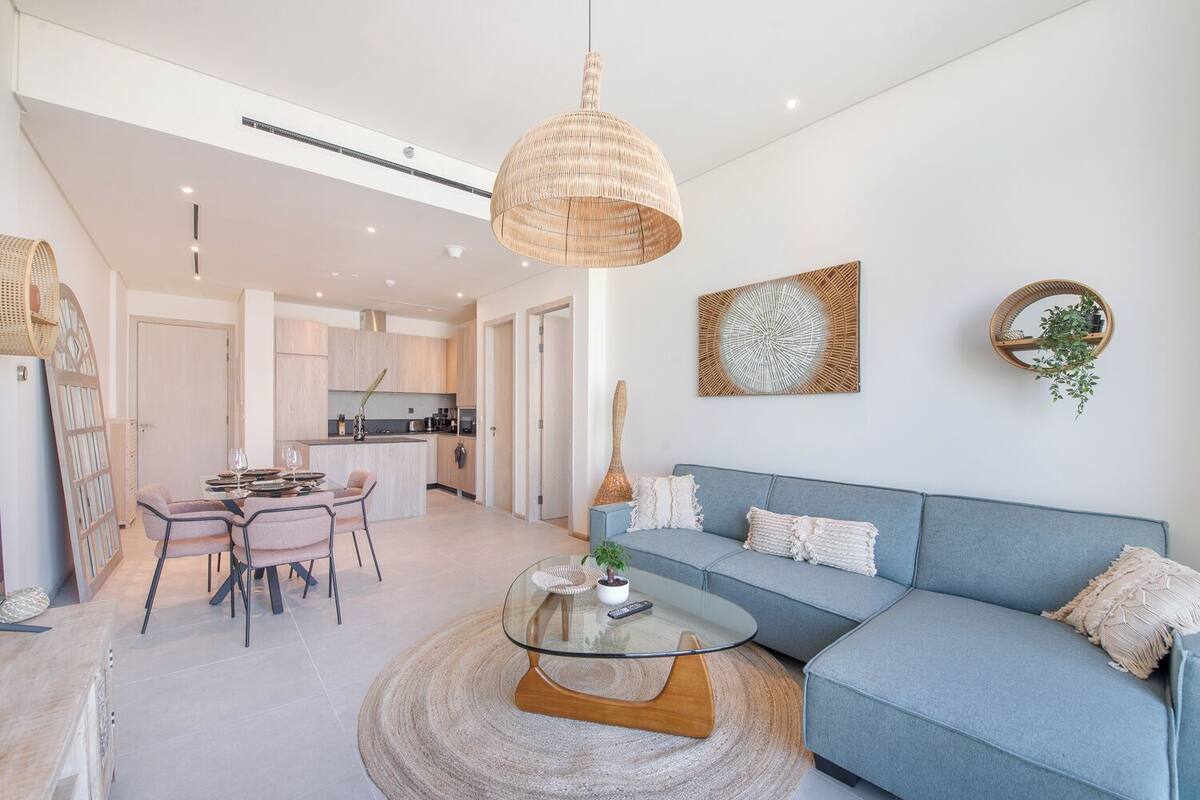 A modern living room with a glass coffee table, a blue sofa, and a dining area with a table and chairs.