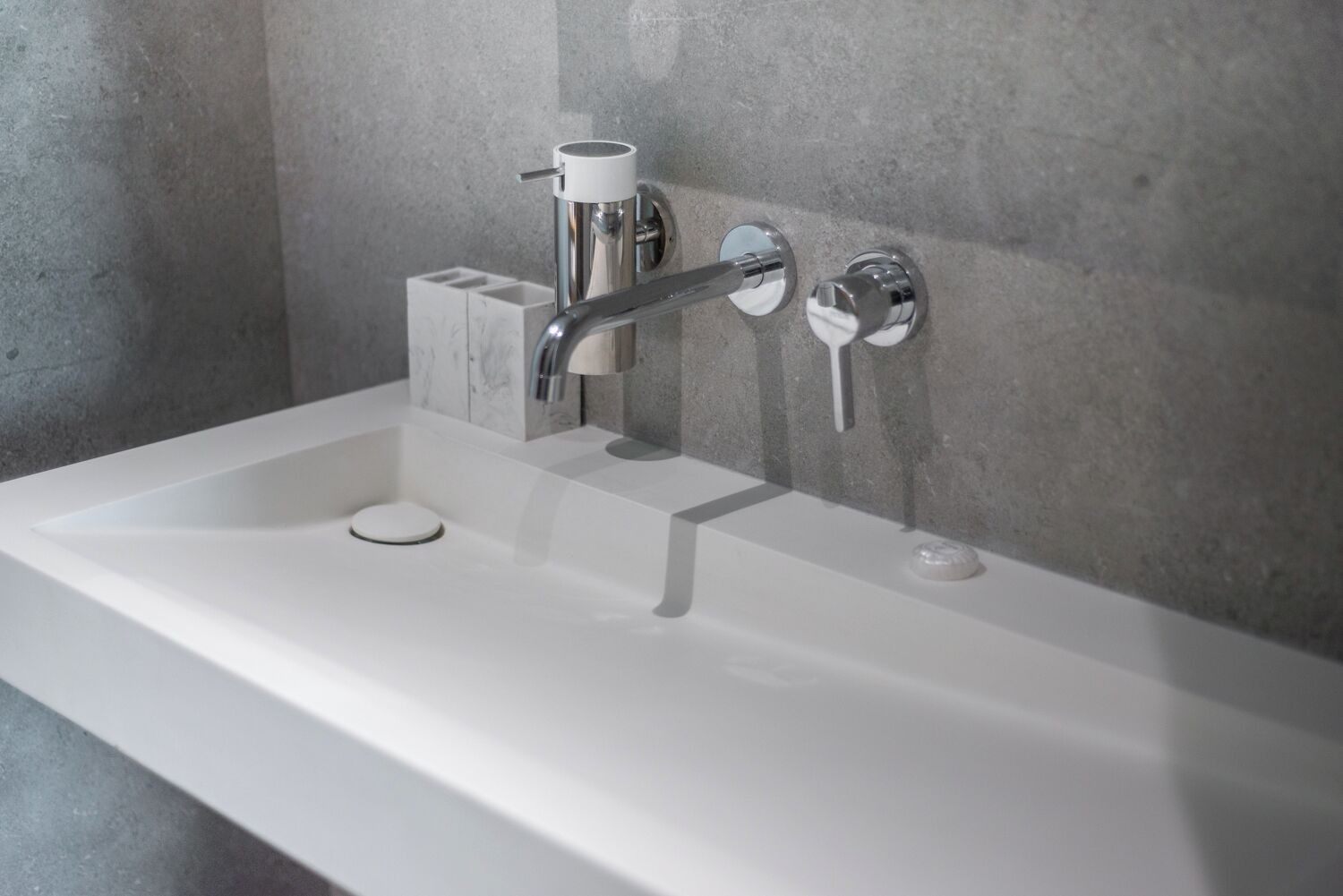 A modern bathroom with a white sink, chrome faucet, and a marble accent wall.