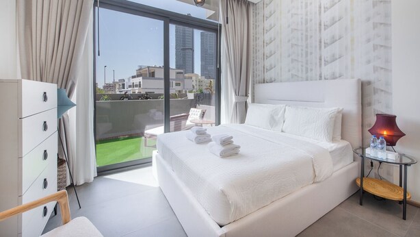 A modern hotel room with a large bed, a glass door leading to a balcony, and a city view. - Czechin - Signature Livings (Madinat Zayed)