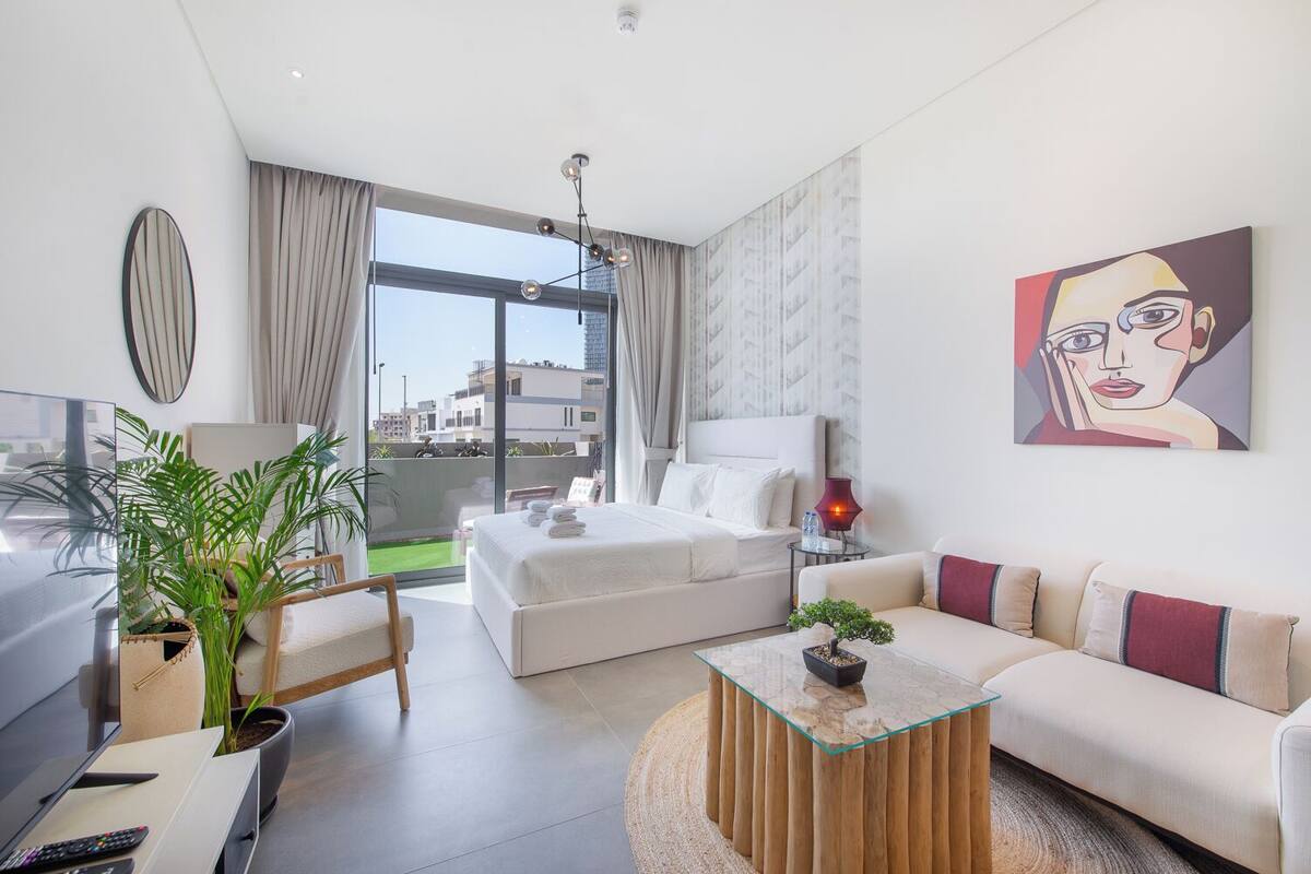 A modern hotel room with a large bed, a sofa, a dining table, and a balcony with a view of the city.