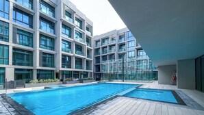 A modern building with a rooftop pool area, featuring a large rectangular pool and a wooden deck. - Czechin - Signature Livings (Madinat Zayed)