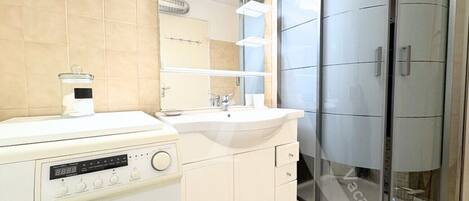 Un baño moderno con lavadora, lavamanos y cabina de ducha de vidrio.