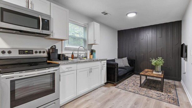 A modern kitchen with white cabinets, a black stove, and a microwave. There's a black sofa and a small wooden table with a plant. - 2 bedroom Rustic Duplex-Free Parking (Lithia Springs)