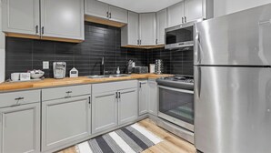 Una cocina moderna con gabinetes grises, un refrigerador de acero inoxidable, horno integrado, cafetera y encimera de madera.