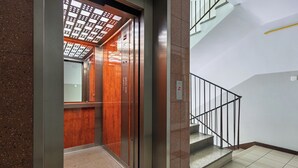 Ένας ανελκυστήρας με επένδυση από ξύλο και μεταλλικό σκελετό, που οδηγεί σε μια σκάλα με μεταλλική κουπαστή.