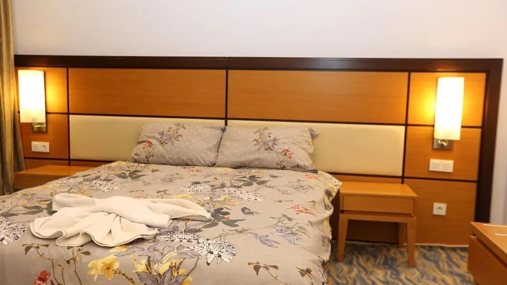 A hotel room with a large bed, floral bedspread, two bedside tables, and wall-mounted lamps.