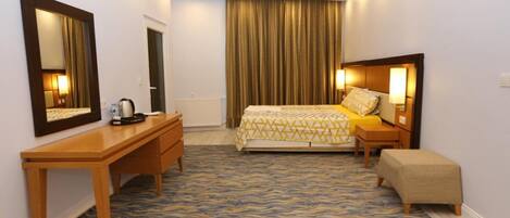 A hotel room with a bed, a desk, a chair, a bench, a mirror, and a curtain.