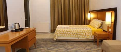 A hotel room with a bed, a desk, a chair, a nightstand, and a mirror.