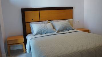 Una cama bien tendida con cabecera de madera, una mesita de noche de madera a un lado y suelo de color claro.