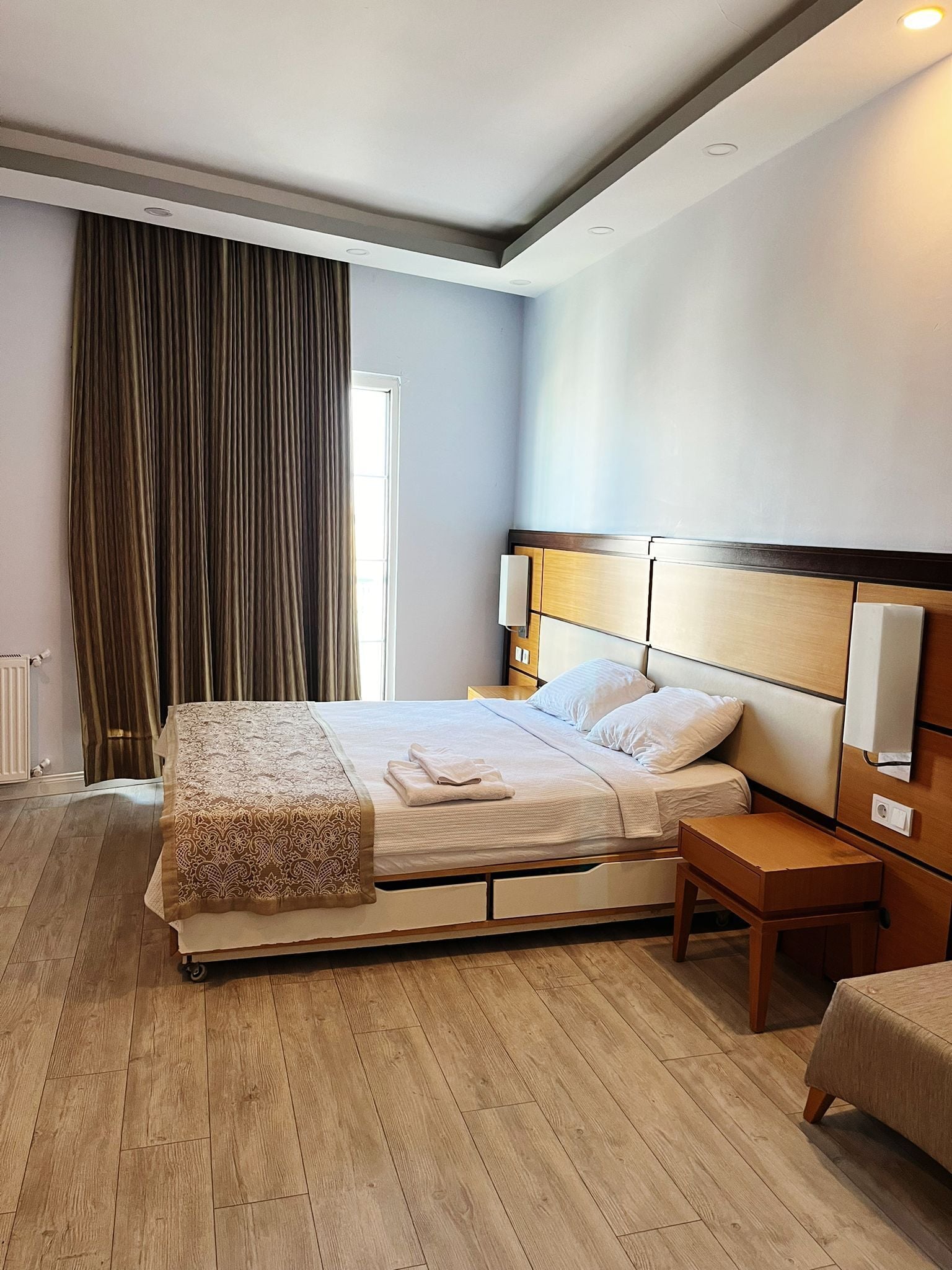 Une chambre d’hôtel avec un grand lit, des tables de chevet, une petite table et une fenêtre avec des rideaux.