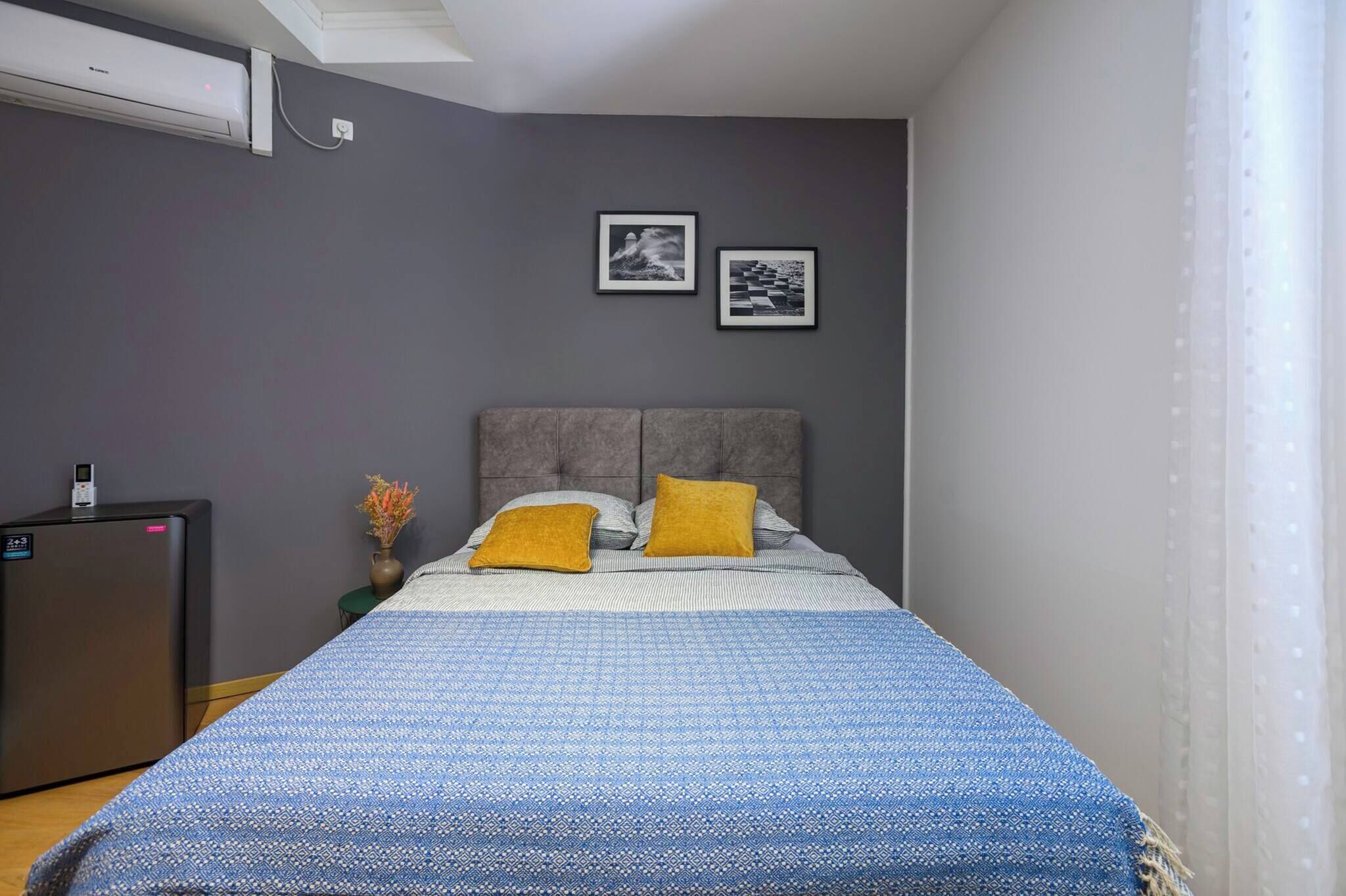 A bedroom with a bed, a nightstand, a desk, and two framed pictures on the wall.