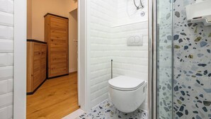 A bathroom with a white toilet, a wooden cabinet, and a shower area with a terrazzo floor. - Vera Studio Deluxe With Oldtown View (Zadar)