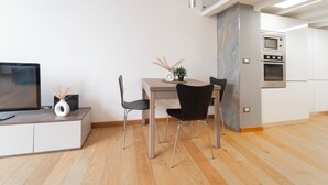 A modern kitchen with white cabinets and stainless steel appliances, a dining area with a wooden table and black chairs, and a flat-screen TV on a white cabinet. - Milan Lambrate M2 Center (Milano)