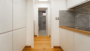 A narrow kitchen with white cabinets, a wooden floor, and a marble backsplash. - Milan Lambrate M2 Center (Milano)