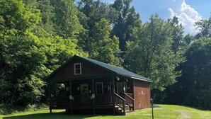 A rustic wooden cabin with a porch, surrounded by lush greenery and a clear sky. - Lowry’s Retreat (South Bloomingville)