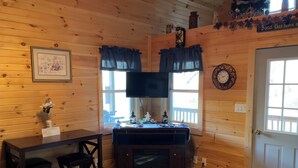 A cozy cabin interior with wooden walls, a dining area with a table and chairs, a fireplace, and a door with a decorative wreath. - Lowry’s Retreat (South Bloomingville)