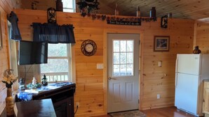 A cozy cabin interior with a wooden interior, a dining area with a table and chairs, a kitchen with a refrigerator, and a door with a sign above it. - Lowry’s Retreat (South Bloomingville)