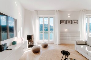 A modern living room with a large TV, a fireplace, and a view of a mountainous landscape through large windows. - Paradise View (Como)