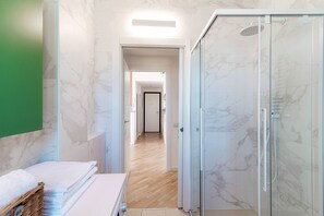 A modern bathroom with a glass shower enclosure, marble walls, and a wooden floor. - Paradise View (Como)