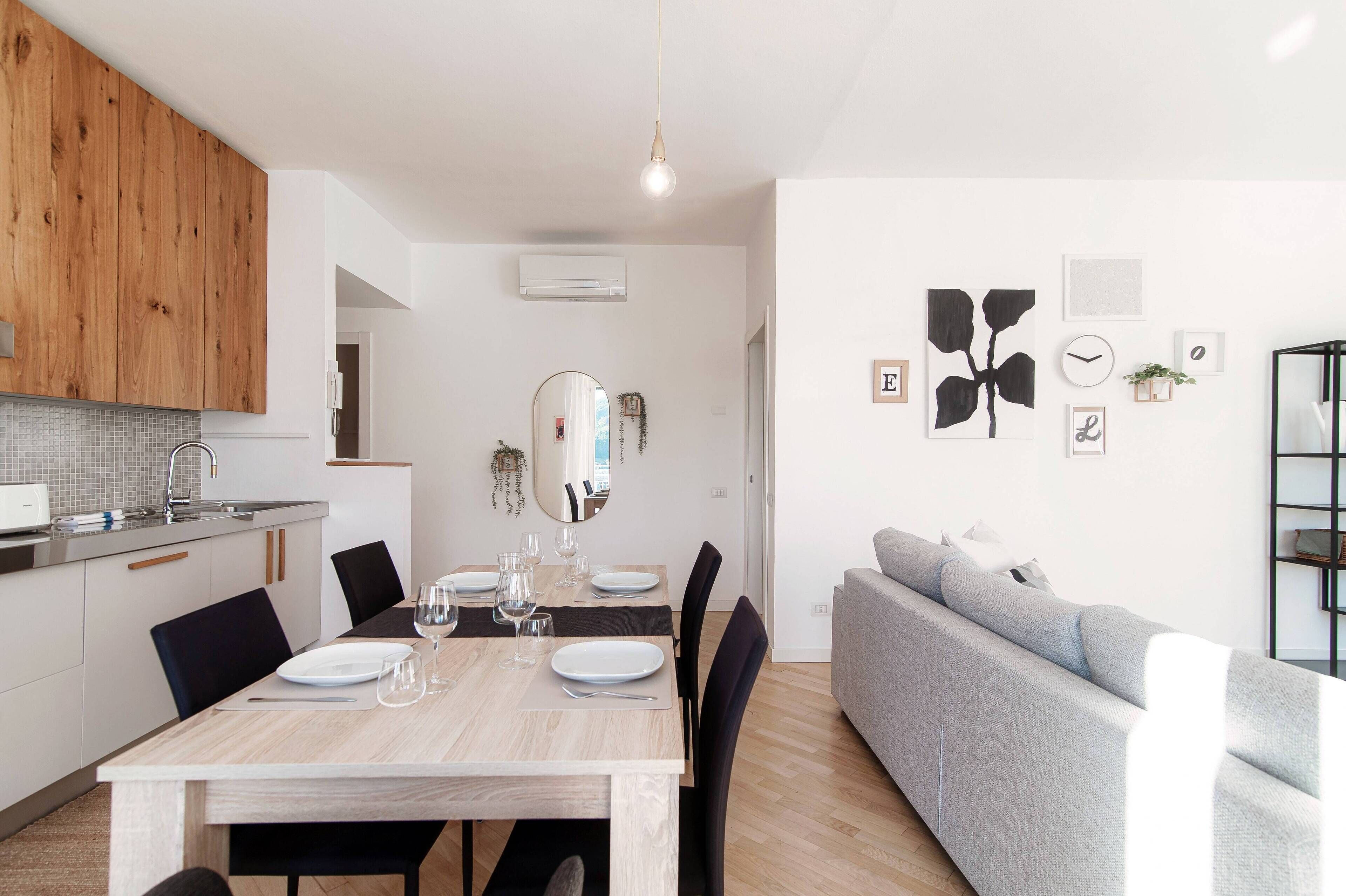 Eine moderne Küche mit Holzschränken, einem Esstisch für vier Personen und einem grauen Sofa im Wohnbereich.