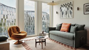 A modern living room with a sofa, armchair, and coffee table. Large windows offer views of a cityscape. - Edgar Suites Lille - Shake  (Lille)