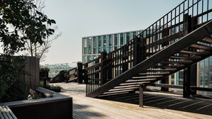 A modern outdoor area with a wooden deck, metal railings, and a staircase leading to a building with large windows. - Edgar Suites Lille - Shake  (Lille)