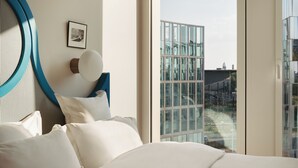 A modern hotel room with a large bed, a view of the city through floor-to-ceiling windows, and a unique blue circular design on the wall. - Edgar Suites Lille - Shake  (Lille)