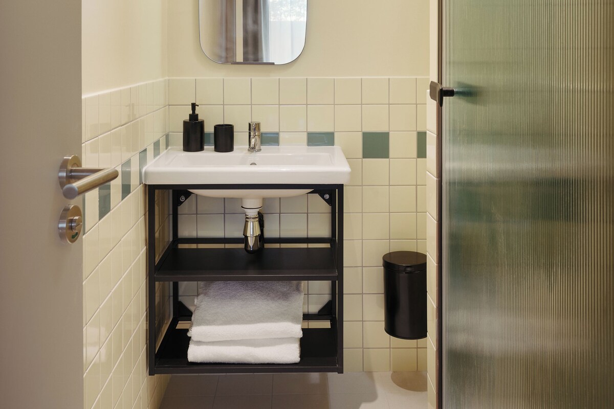 A bathroom with a white sink, a mirror, a towel rack, and a trash can.