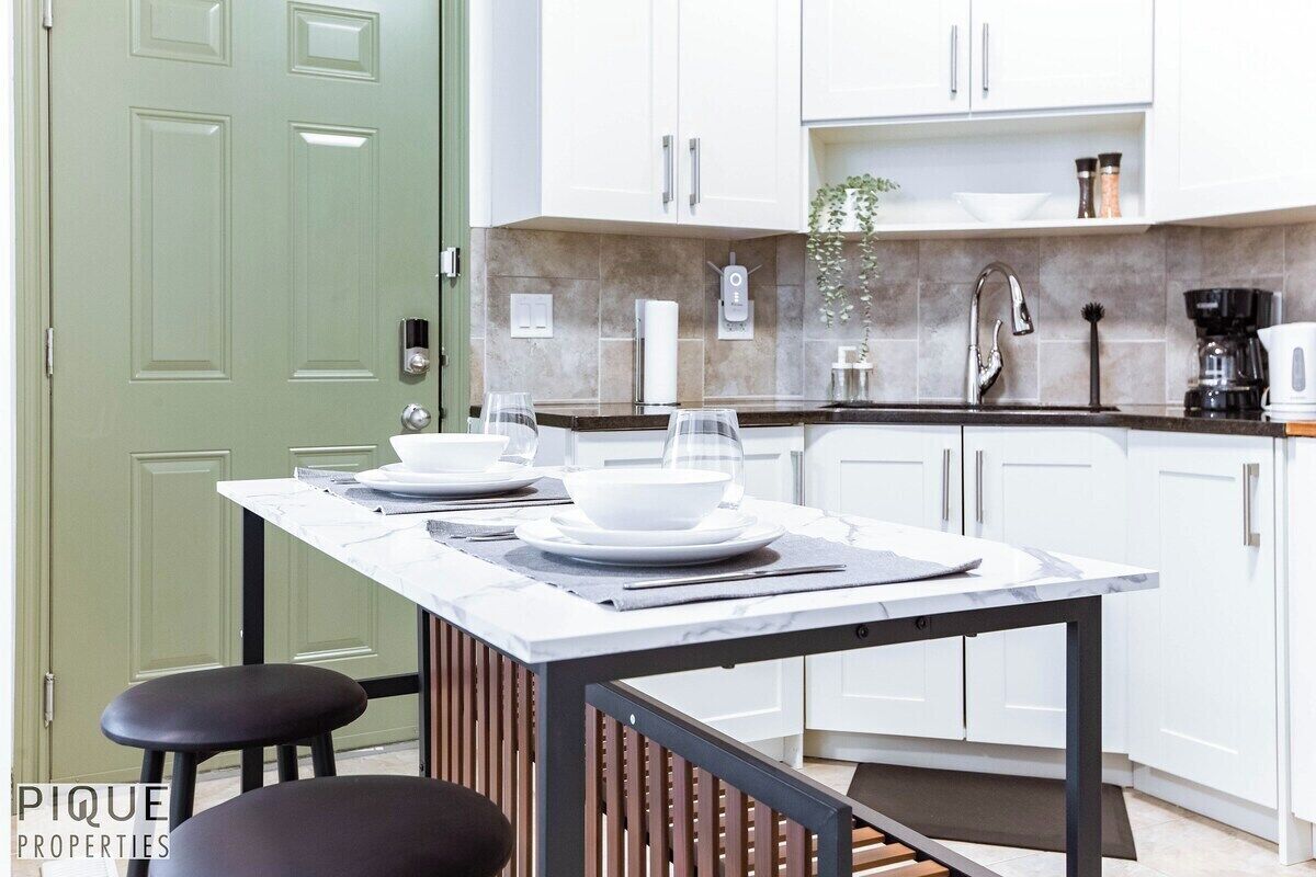 A modern kitchen with white cabinets, a marble countertop, and a green door.