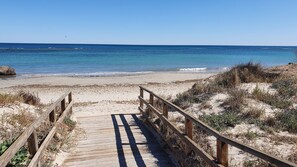 A wooden boardwalk leading to a sandy beach with clear blue water.