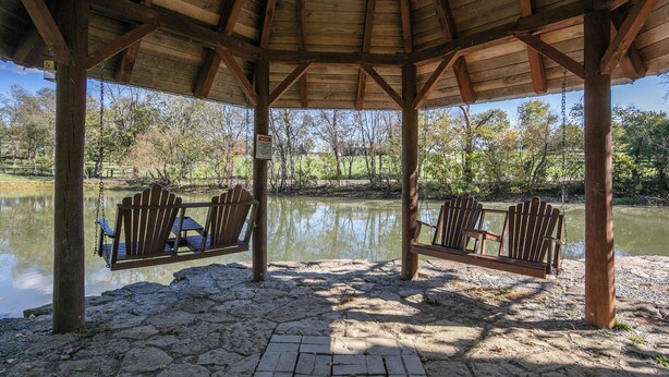 A wooden gazebo with two swings over a pond, surrounded by trees and a clear sky. - Scenic Stillwater Retreat in rural KY Horse Country, WiFi/AC, Fishing/Canoeing (Georgetown)