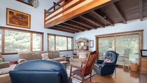 A spacious living room with wooden beams, large windows, and comfortable seating including a blue chair and a rocking chair. - Scenic Stillwater Retreat in rural KY Horse Country, WiFi/AC, Fishing/Canoeing (Georgetown)