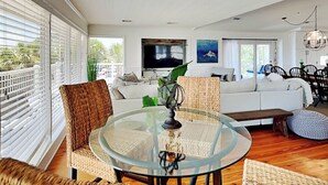 A modern living room with a glass coffee table, wicker chairs, a white sofa, and a TV mounted on the wall. - Oceanside Unit A | Luxe Beachfront! (Tybee Island)