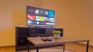 A modern living room with a flat-screen TV, a wooden coffee table, a small potted plant, and a dark-colored entertainment unit. - Modern apartment in Recoleta (Cochabamba)