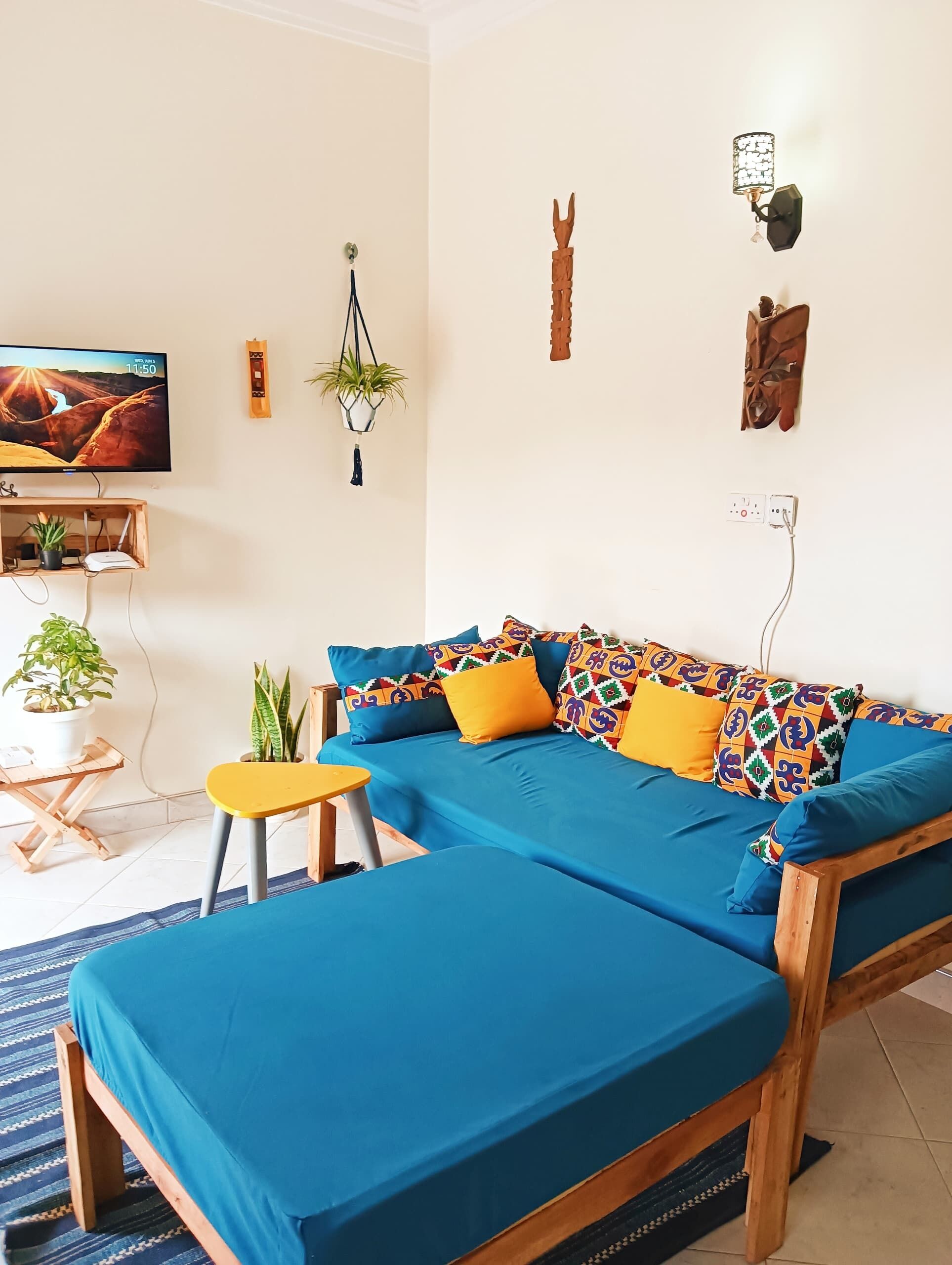 A modern living room with a blue sofa, colorful cushions, a small wooden table, and a TV on the wall.