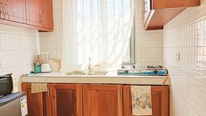 A kitchen with wooden cabinets, a white tiled backsplash, a window with sheer curtains, a stove, and a sink. - Sawe Homes 4&5 (Kampala)