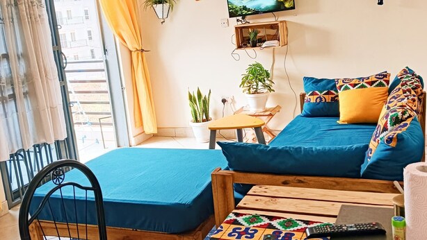 A living room with a sofa, a chair, a small table, and a TV on the wall. - Sawe Homes 4&5 (Kampala)