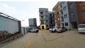 A multi-story residential building with a central entrance, parking spaces, and a gated driveway. - Sawe Homes 4&5 (Kampala)