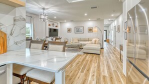 A spacious kitchen with a marble countertop, a dining area with a table and chairs, a living room with a sofa and a coffee table, and a hallway with a refrigerator. - Charming 3-bedroom Relaxing Family Vacation Retreat On The Water,  Fishing (Rotonda West)
