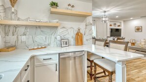 A modern kitchen with marble backsplash, wooden shelves, and a dining area with a long table and chairs. - Charming 3-bedroom Relaxing Family Vacation Retreat On The Water,  Fishing (Rotonda West)