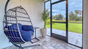 A hanging chair with blue cushions, a potted plant, and a view of a green field through a glass door. - Charming 3-bedroom Relaxing Family Vacation Retreat On The Water,  Fishing (Rotonda West)