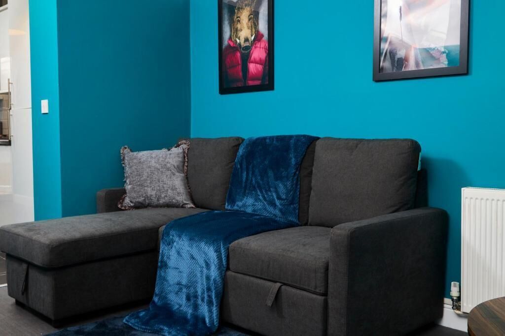 A grey sofa with a blue throw blanket, a grey pillow, and a framed picture of a horse on a teal wall.