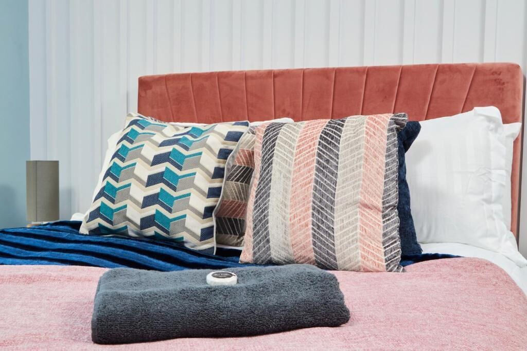 A bed with a red upholstered headboard, multiple patterned pillows, and a grey throw blanket.