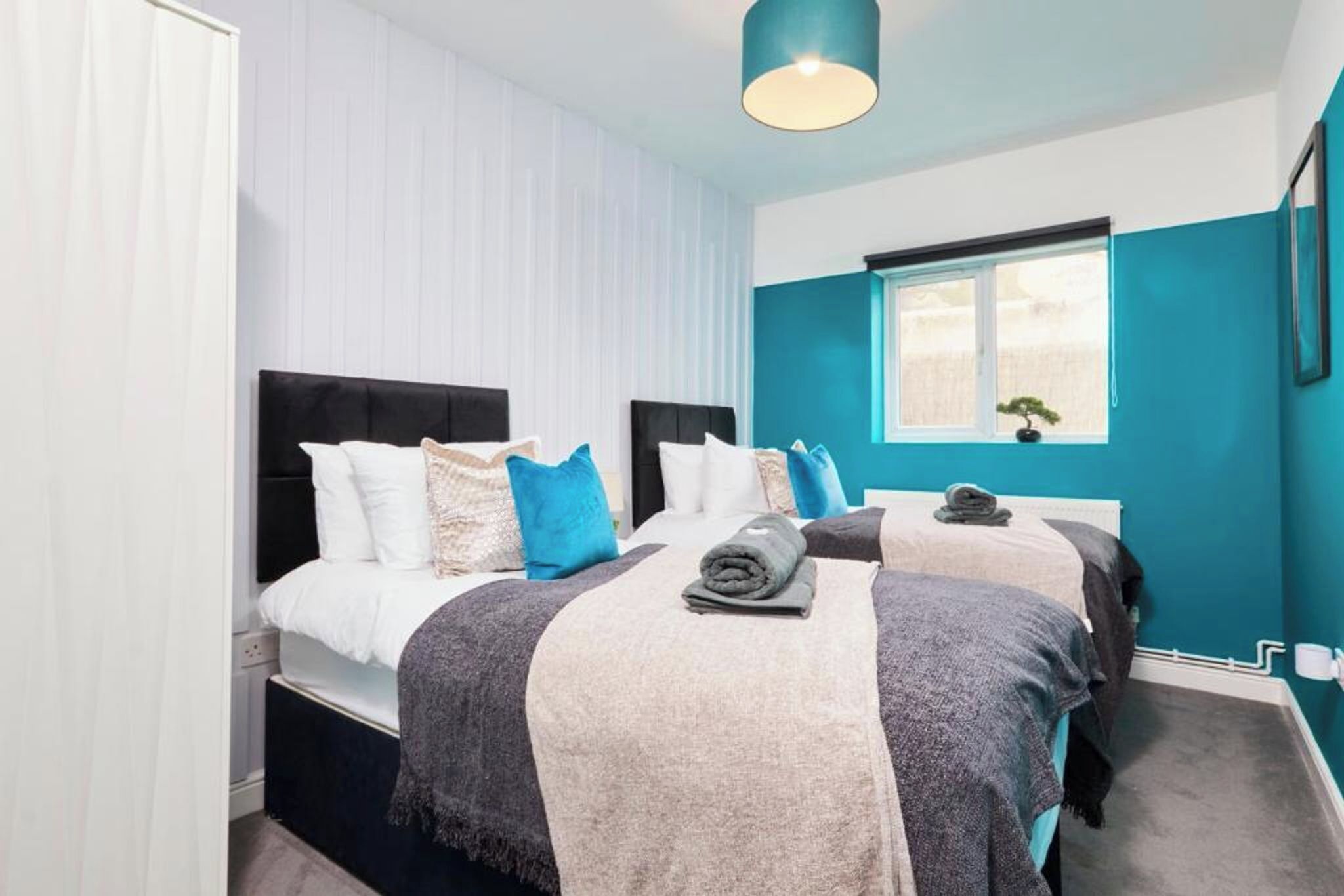 A hotel room with two beds, a window, and a ceiling light.
