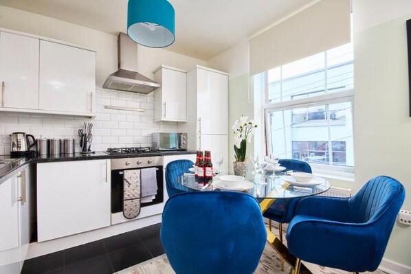 Una cocina moderna con armarios blancos, encimera negra y una silla azul.