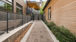 A narrow pathway leading to a building with a wooden facade and a metal fence on one side. - Modern Elegance on Linden – Walk/Bike Everywhere! (Fort Collins)